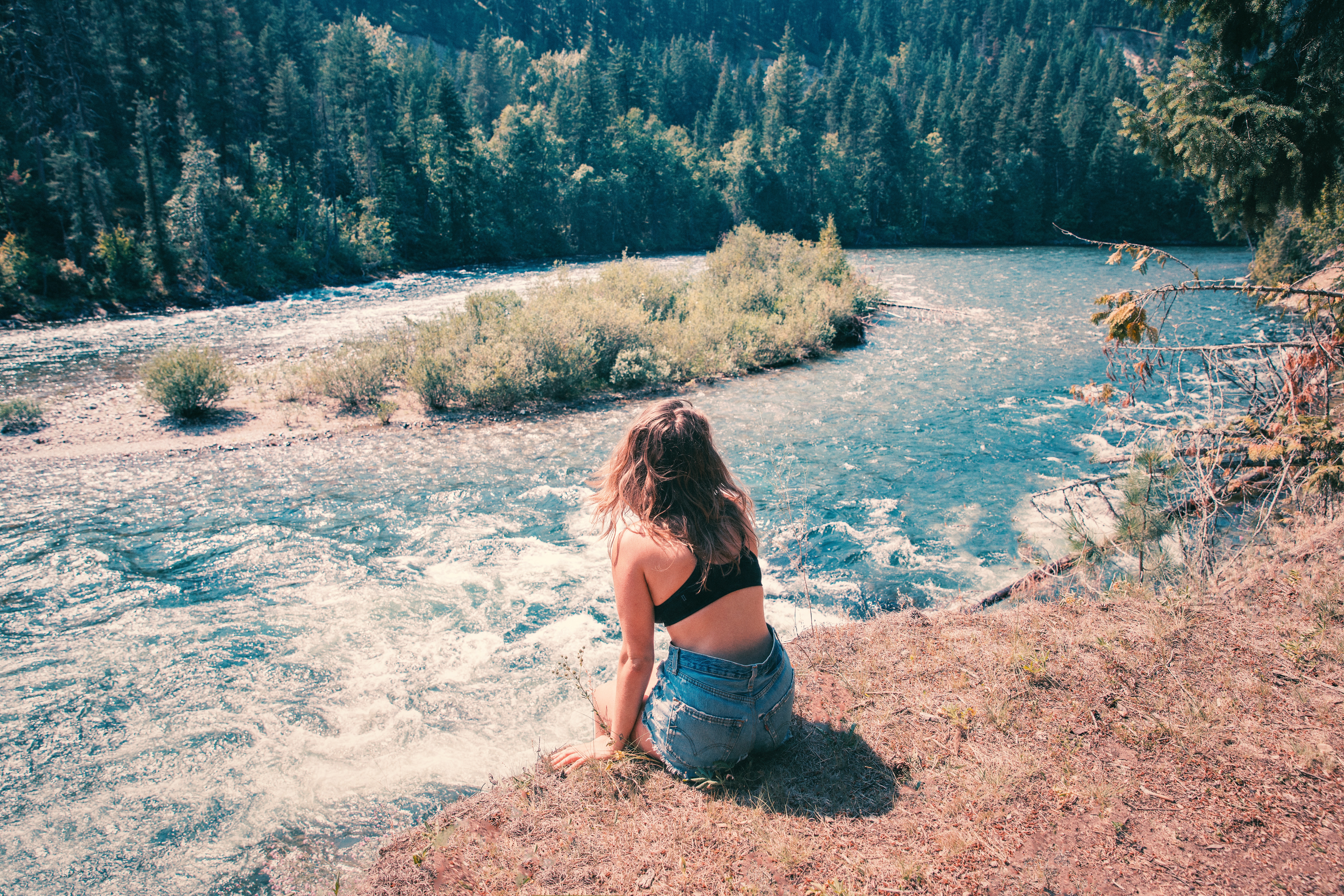 woman sitting on a clif overlooking a river in the mountains reflecting on her thoughts about her life